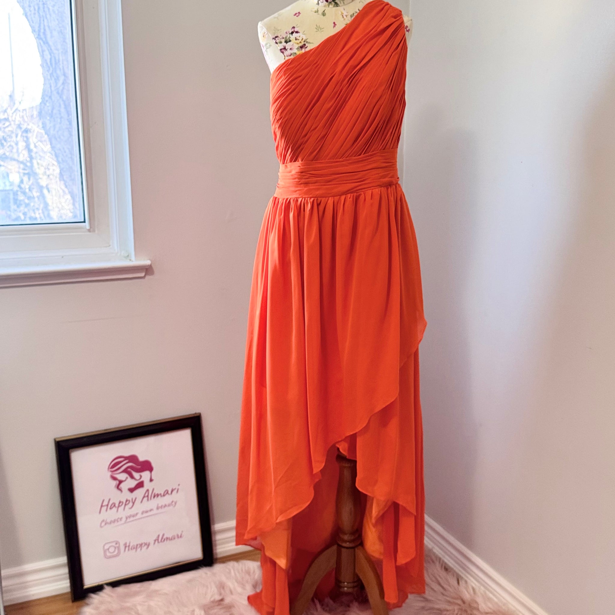 Turn heads with this stunning one-shoulder asymmetrical gown in a bold, fiery orange hue! Designed to make a statement, this dress features intricate pleating across the bodice for a flattering fit, a cinched waist that accentuates your curves, and a flowing high-low skirt that moves beautifully with every step.